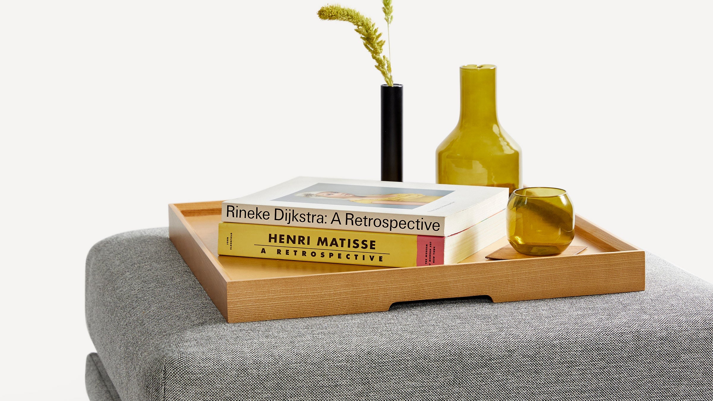 a gray couch with a wooden tray holding books, a vase, and a yellow vase on top