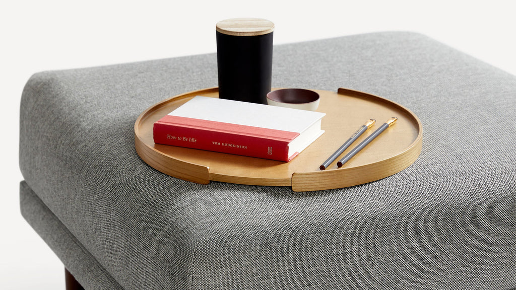 a gray ottoman with a wooden tray, a pen, and a notebook on it