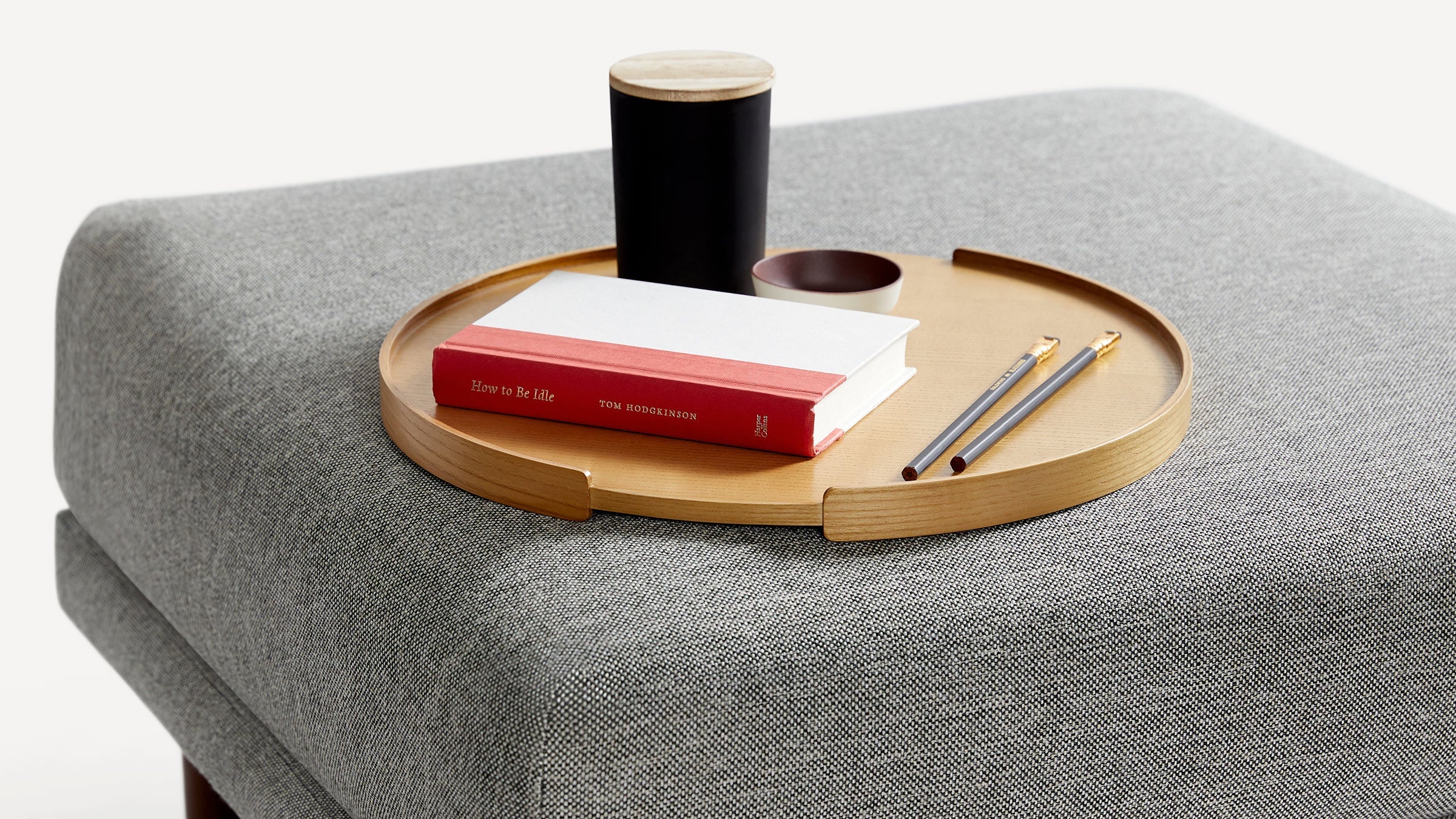 a gray ottoman with a wooden tray, a pen, and a notebook on it