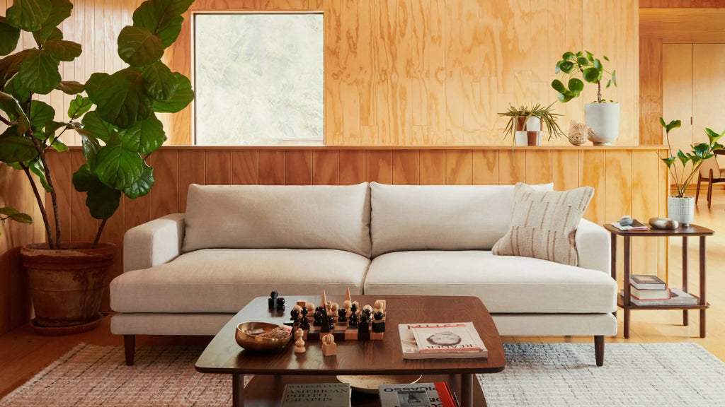 Light beige modern sofa with a textured pillow in a wooden-paneled living room, accompanied by a coffee table and side table.