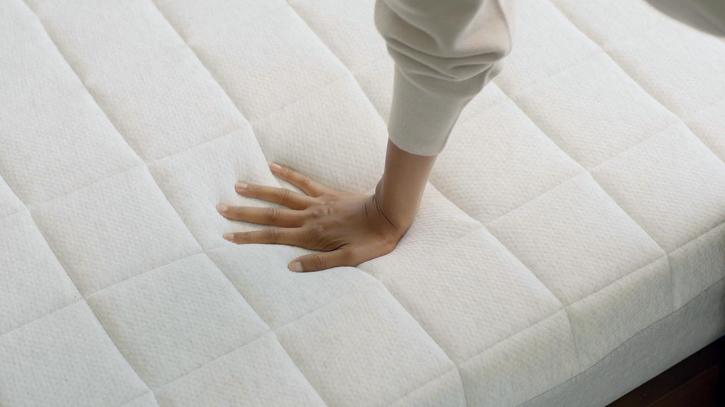 A hand pressing down on a white quilted mattress, showing its softness and cushioning effect.