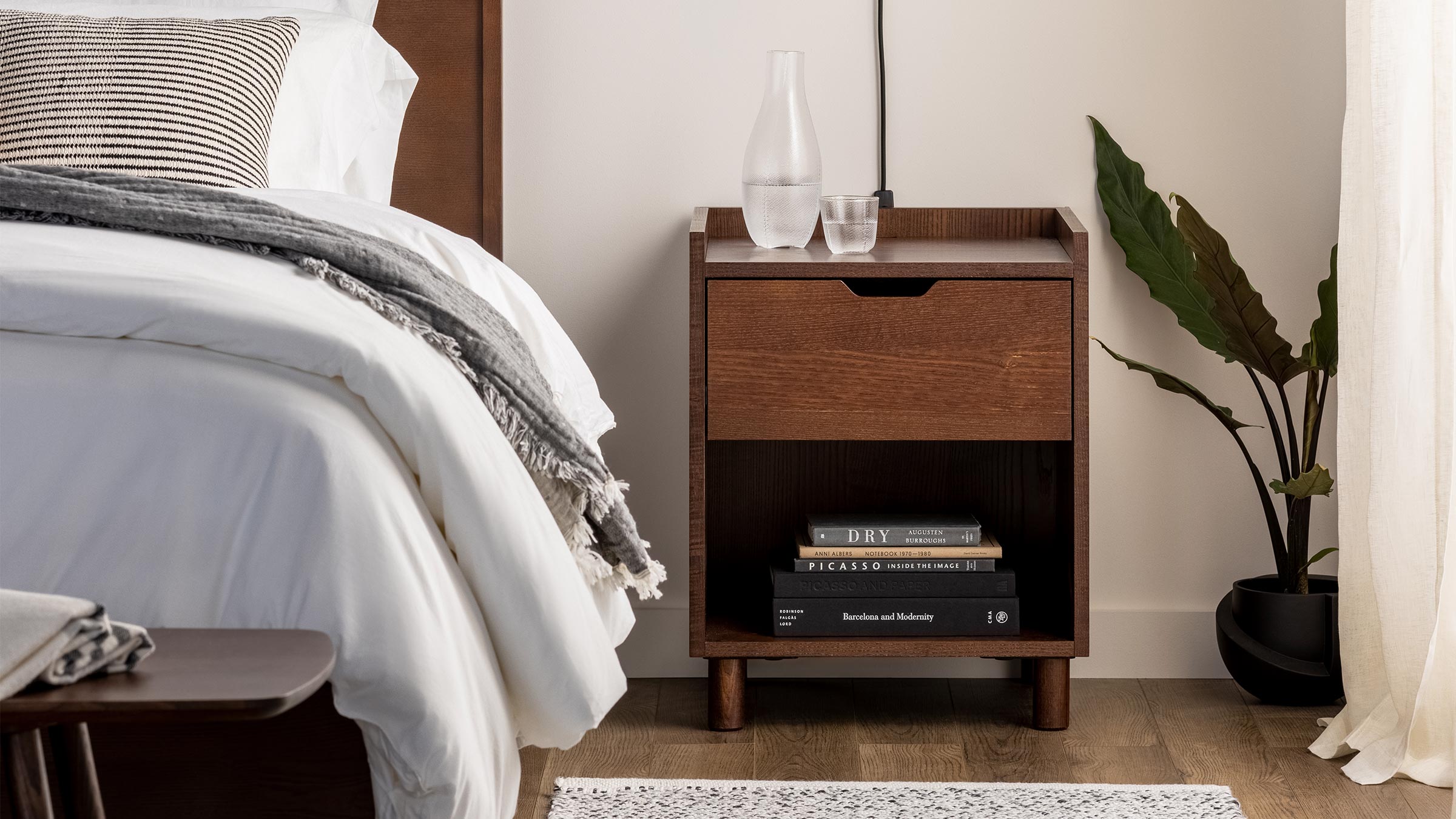 a nightstand with a book, a lamp, and a plant on it