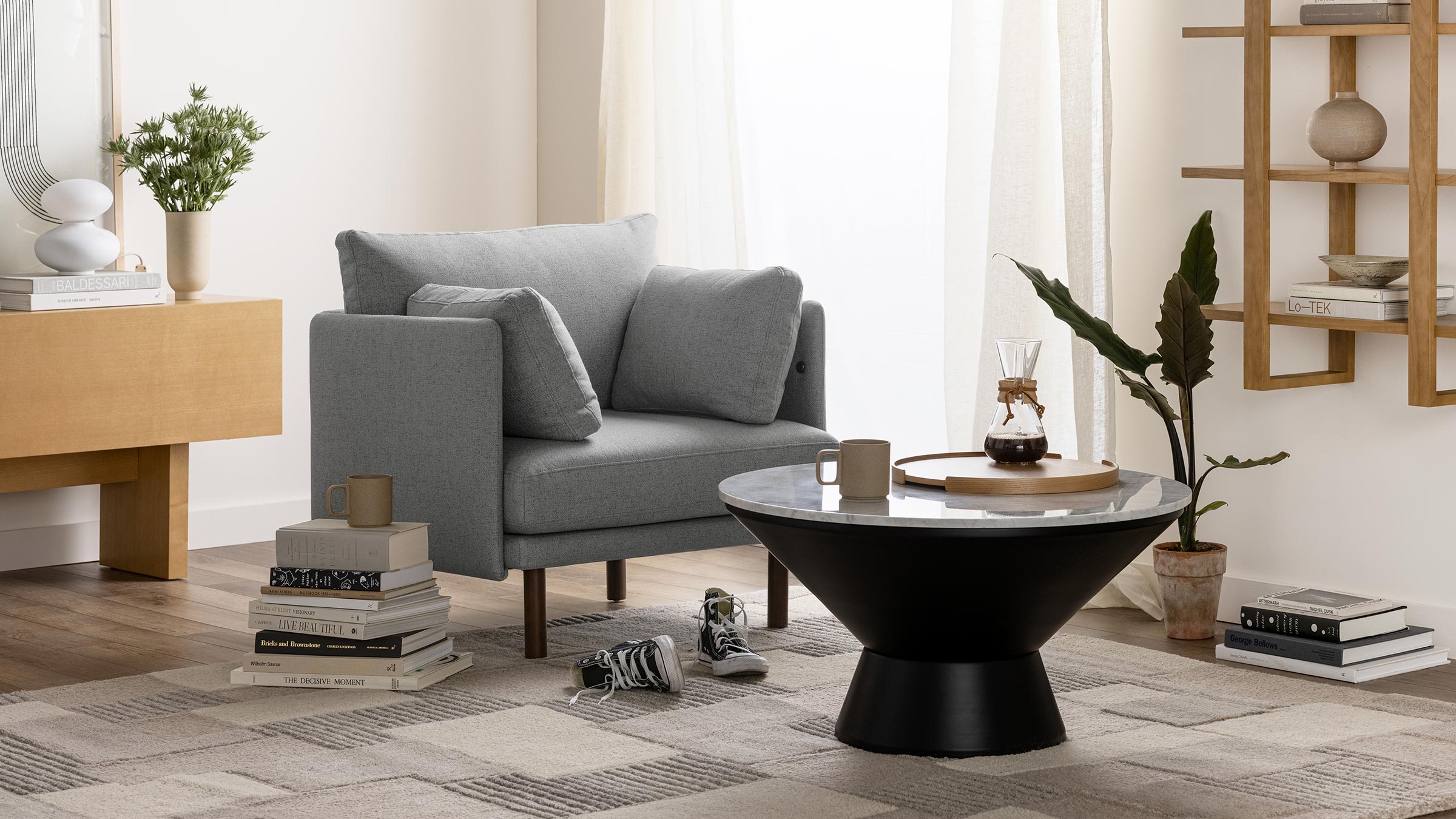 Modern living room featuring a gray armchair, black and white round coffee table, and decorative plants with books.