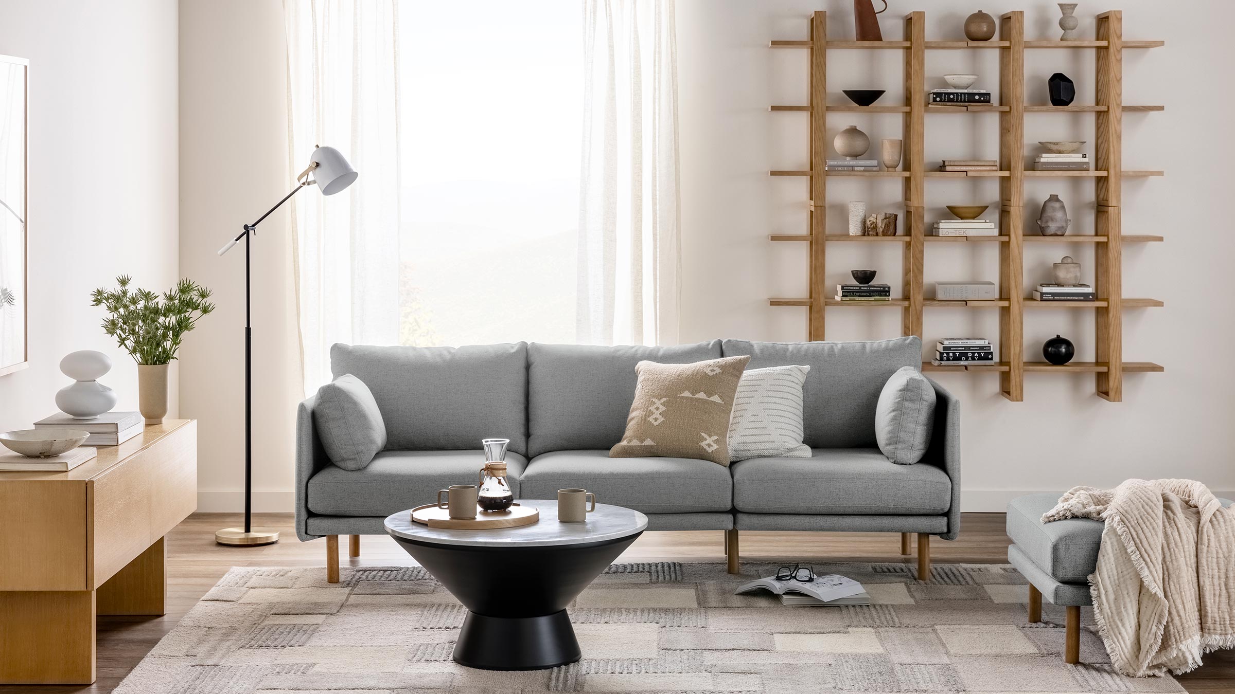 Modern living room with a light gray sofa, round black coffee table, wooden shelving, and cozy neutral-toned decor.