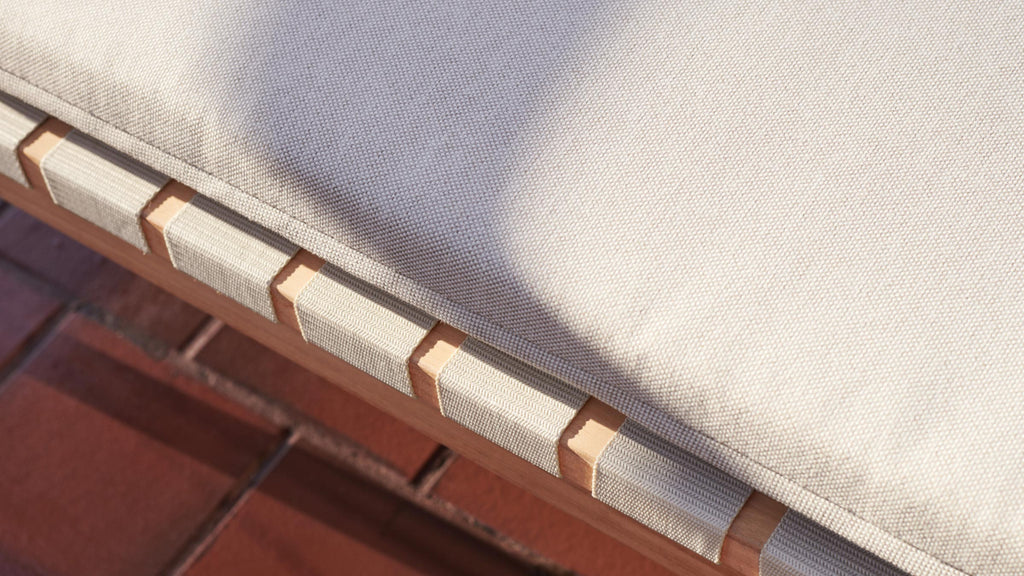 Close-up of a beige fabric cushion with wooden frame and woven fabric straps on a tiled floor background.