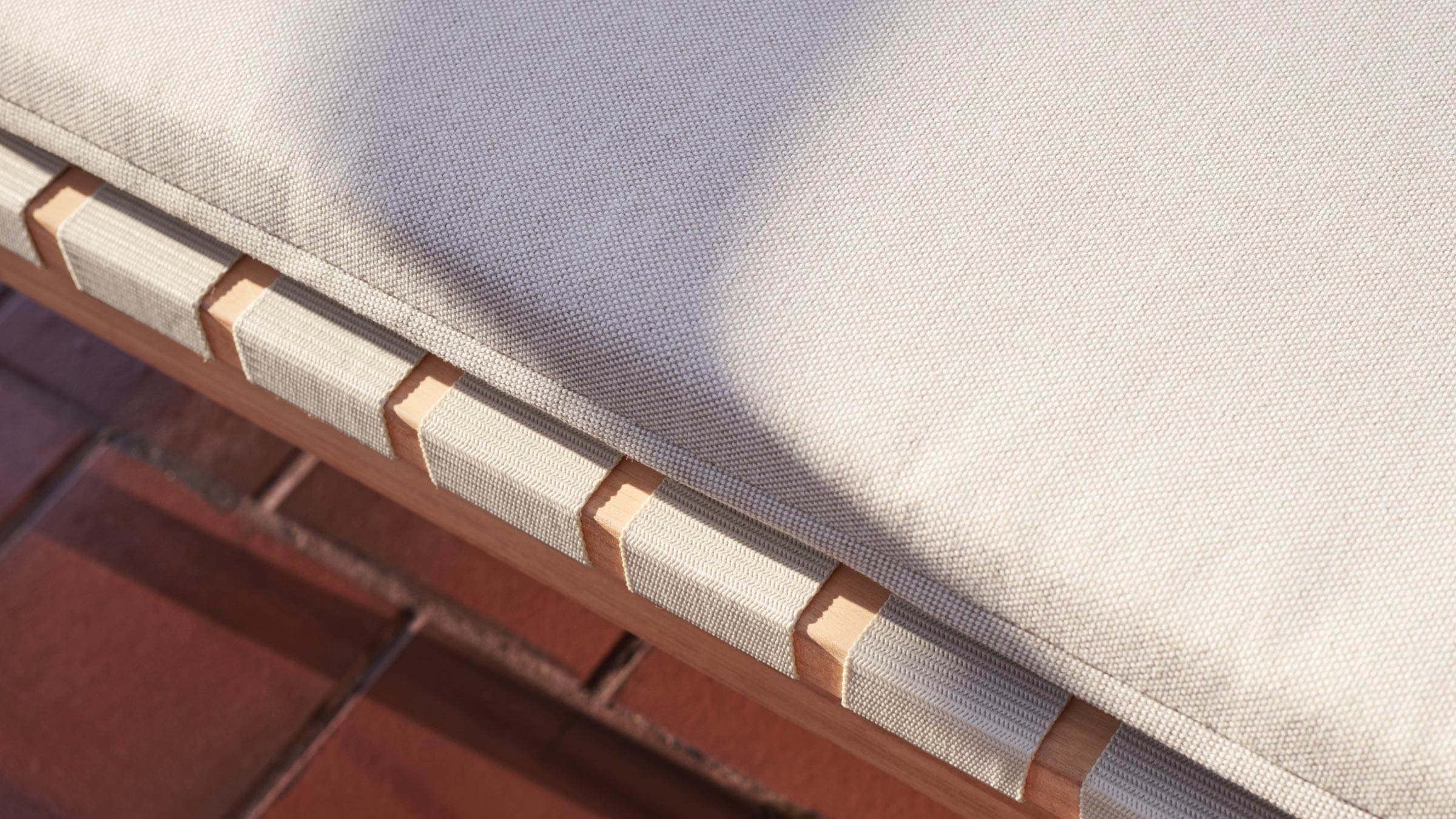 Close-up of a beige fabric cushion with wooden frame and woven fabric straps on a tiled floor background.