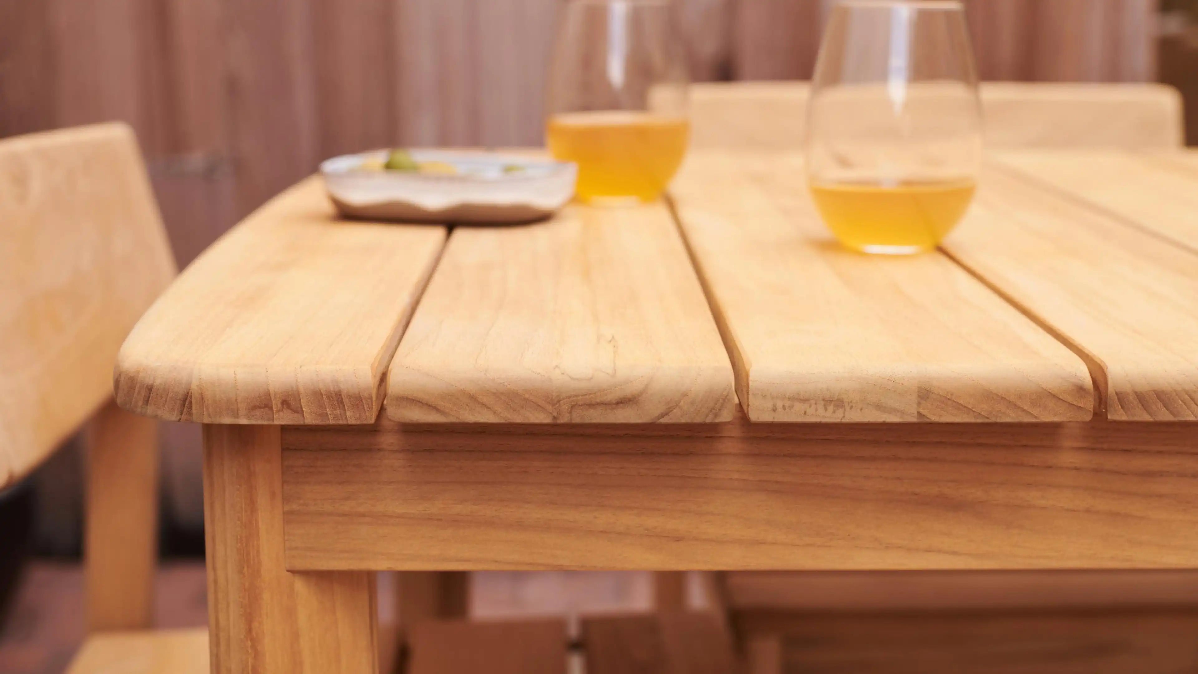 Close-up of a light wooden table with matching chairs, featuring a tray and two glasses with amber liquid.