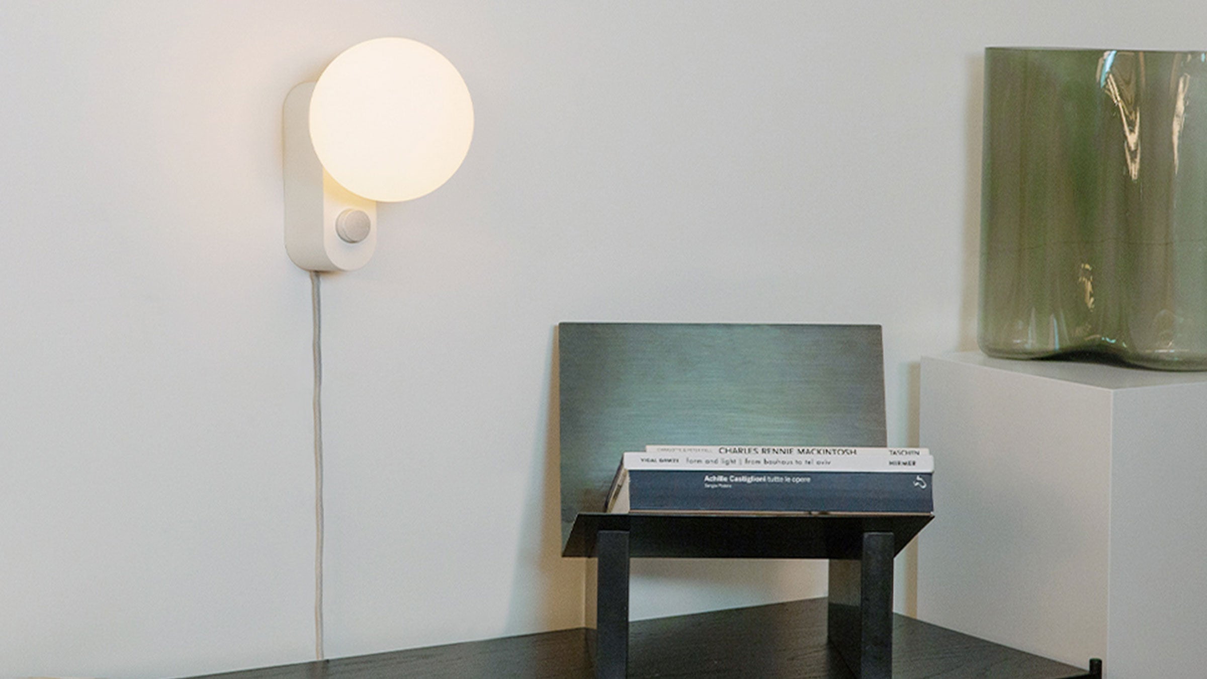 Minimalist white wall-mounted lamp with a round frosted glass shade and adjustable metal arm, illuminating modern interior.