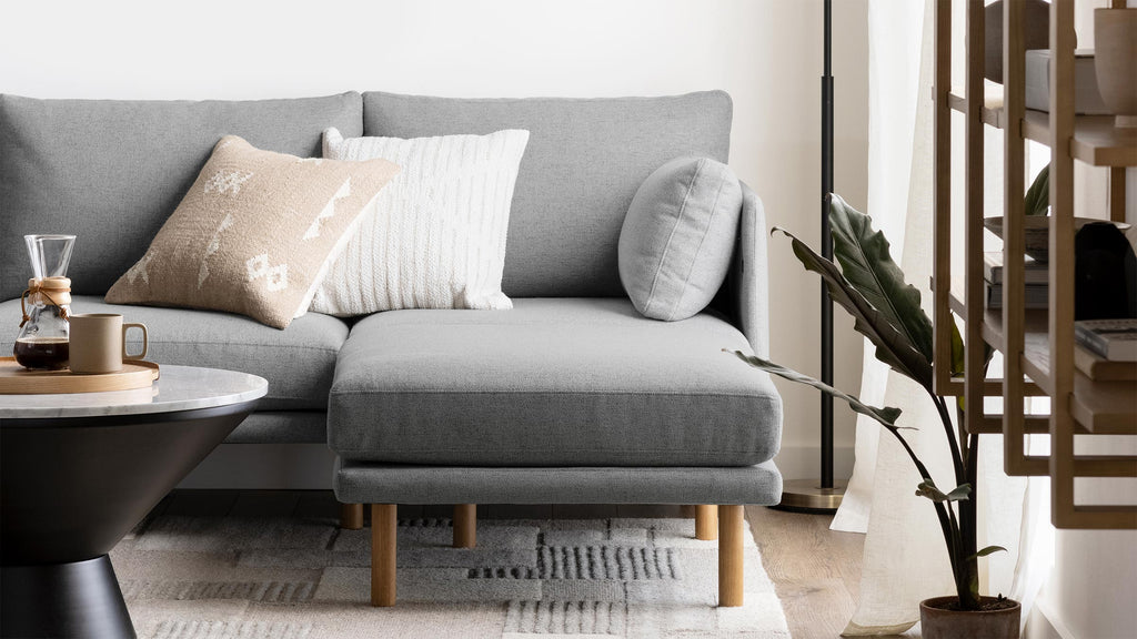 Light gray sectional sofa with wooden legs, decorative pillows, a round black and white coffee table, and a green potted plant nearby.