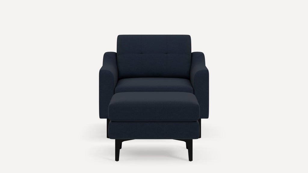 Front view of a modern navy blue upholstered armchair with a matching ottoman and black legs on a white background.