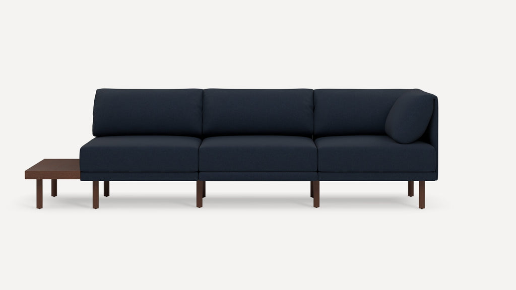 Modern navy blue sectional sofa with wooden legs and attached dark wood side table on one end.
