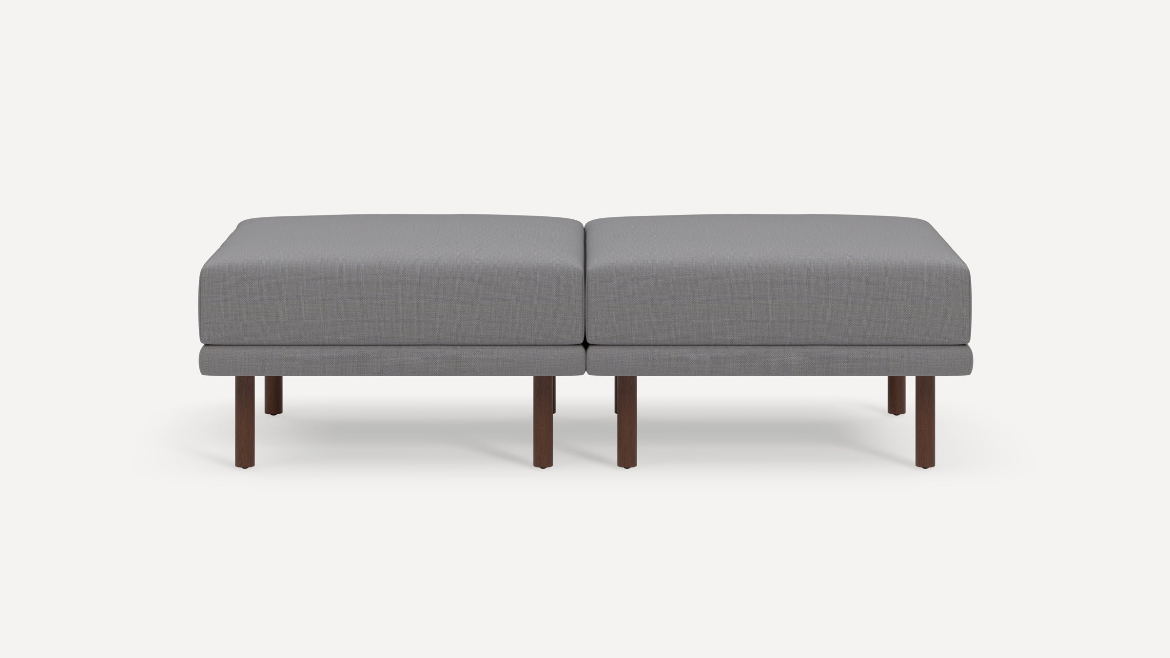 Modern gray fabric ottoman bench with two cushioned seats and dark wooden legs, featuring a sleek and minimalist design.