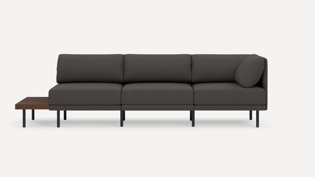 Modern dark gray three-seater sofa with slim black legs and attached wooden side table on left side.