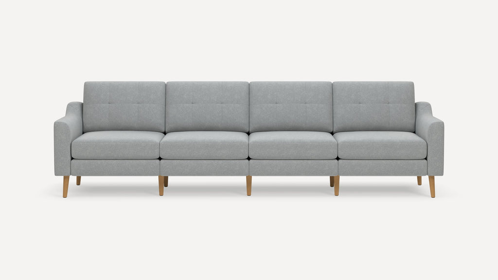 Modern light gray fabric four-seater sofa with tufted back cushions and wooden legs, against a plain white background.