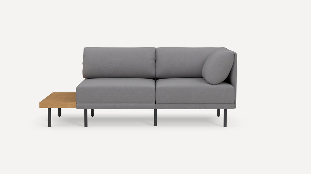 Modern grey L-shaped sectional sofa with black metal legs and a built-in wooden side table on the left side.