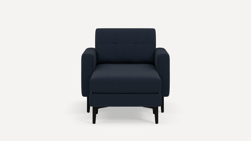 Front view of a modern dark blue upholstered armchair with matching ottoman and black wooden legs on a white background.