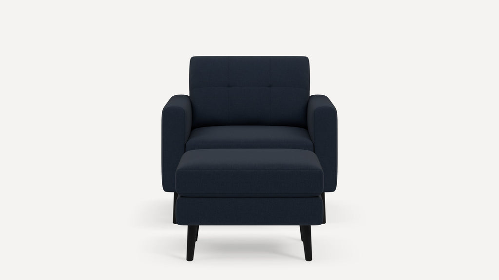 Front view of a modern dark blue armchair with tufted backrest and matching ottoman on black tapered legs.