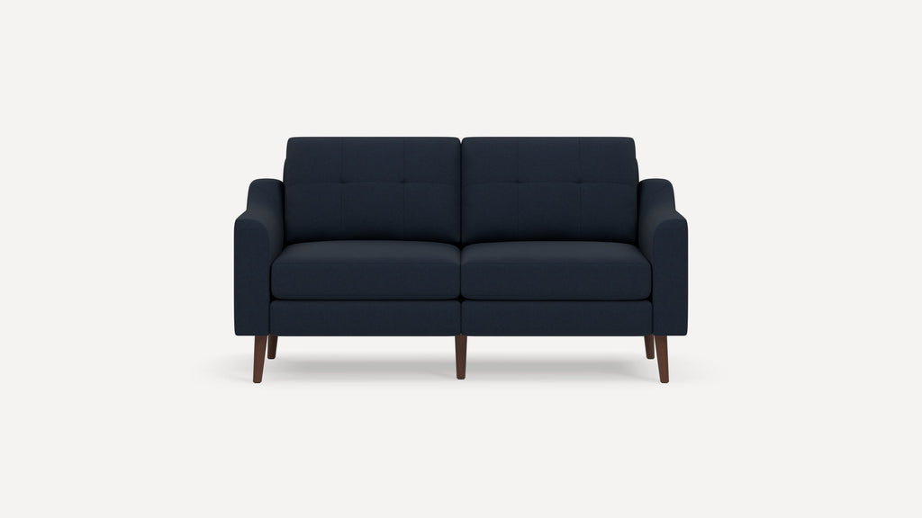 Mid-century modern navy blue two-seater sofa with tufted cushions and dark wooden tapered legs on plain white background.