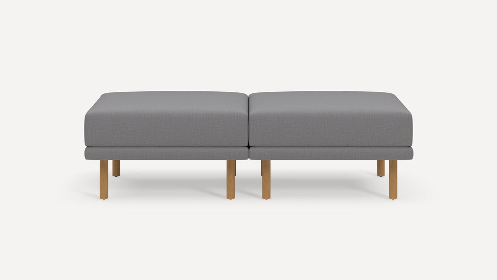Modern gray upholstered bench with wooden legs, featuring two connected cushioned seats and clean, minimalist design.