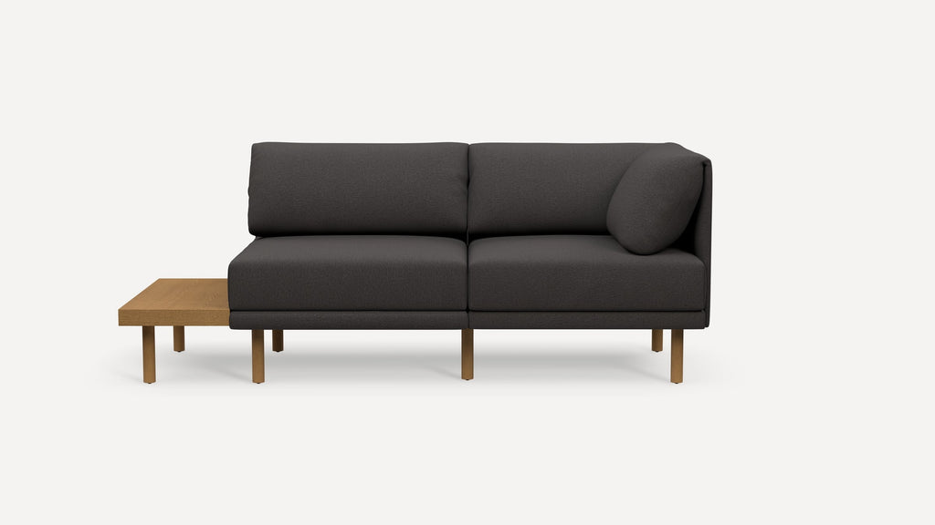 Dark gray modern sofa with wooden legs and a built-in light brown wooden side table attached on the left side.
