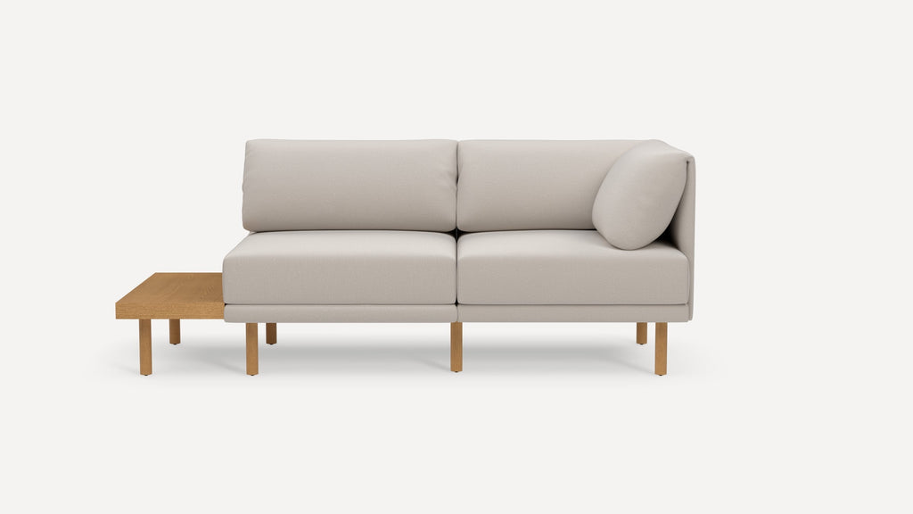Modern beige fabric corner sofa with wooden legs and an integrated wooden side table on the left.