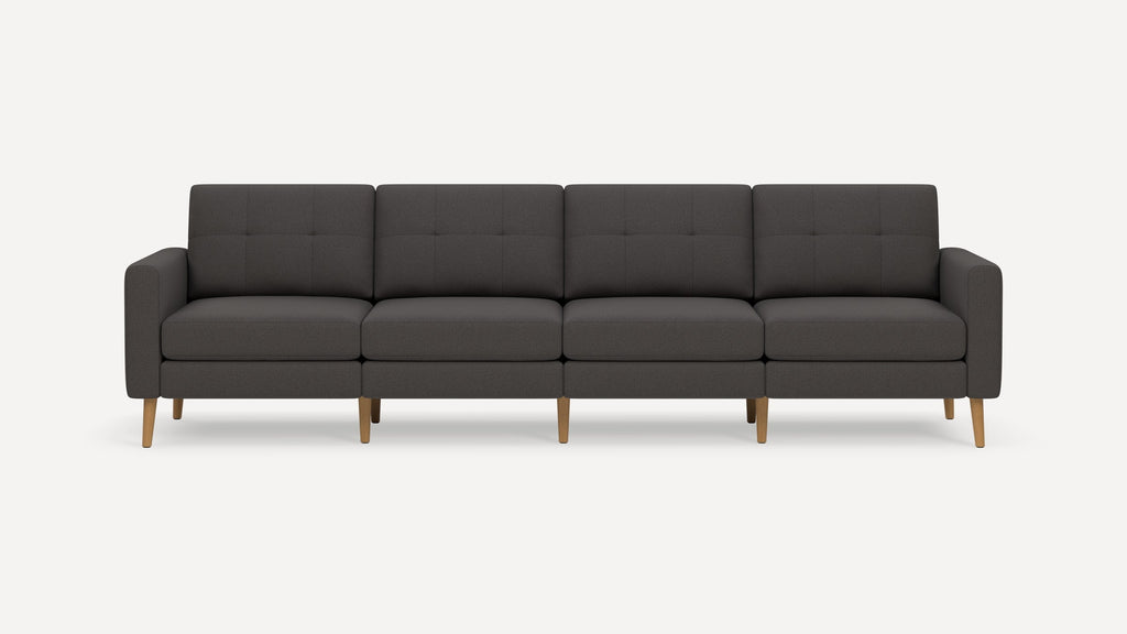 Four-seat dark gray upholstered sofa with tufted back cushions and light wooden tapered legs on a plain white background.