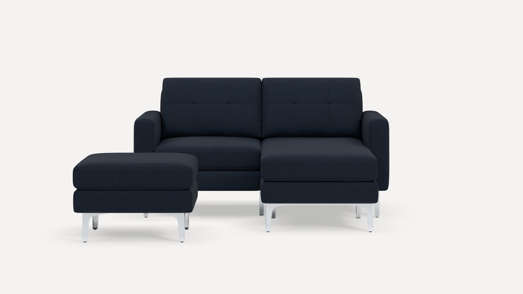 Modern navy blue fabric sectional sofa with matching ottoman, tufted cushions, and sleek silver metal legs against white background.