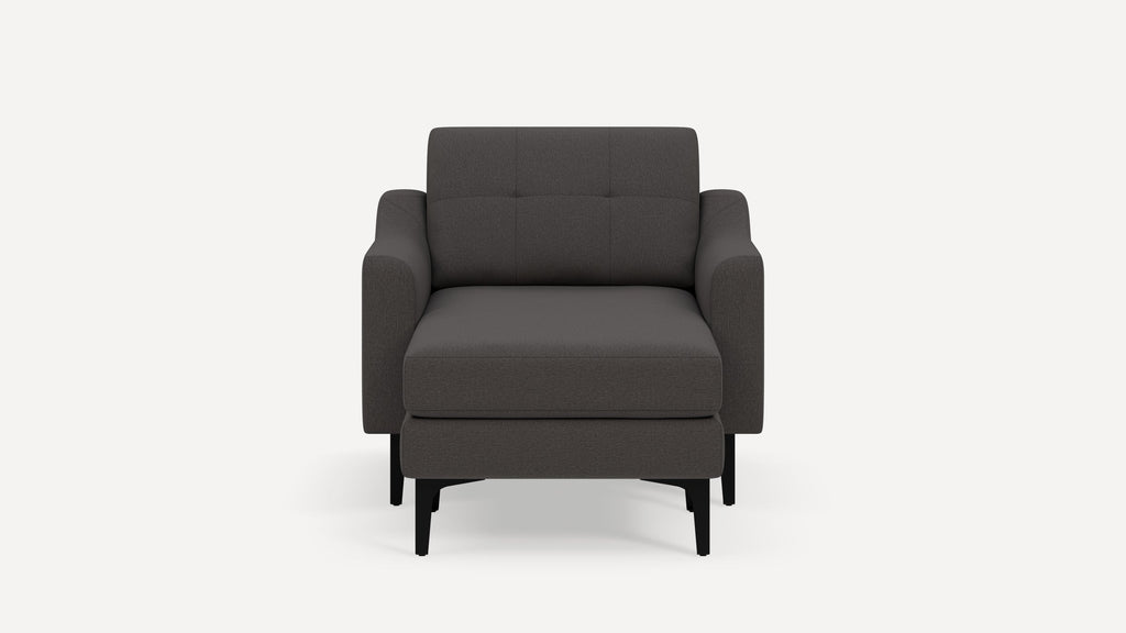 Modern dark gray upholstered armchair with matching ottoman, square tufted back, and black wooden legs on white background.