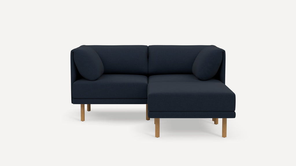 Modern navy blue sectional sofa with wooden legs and two round bolster pillows, designed for comfort and style.
