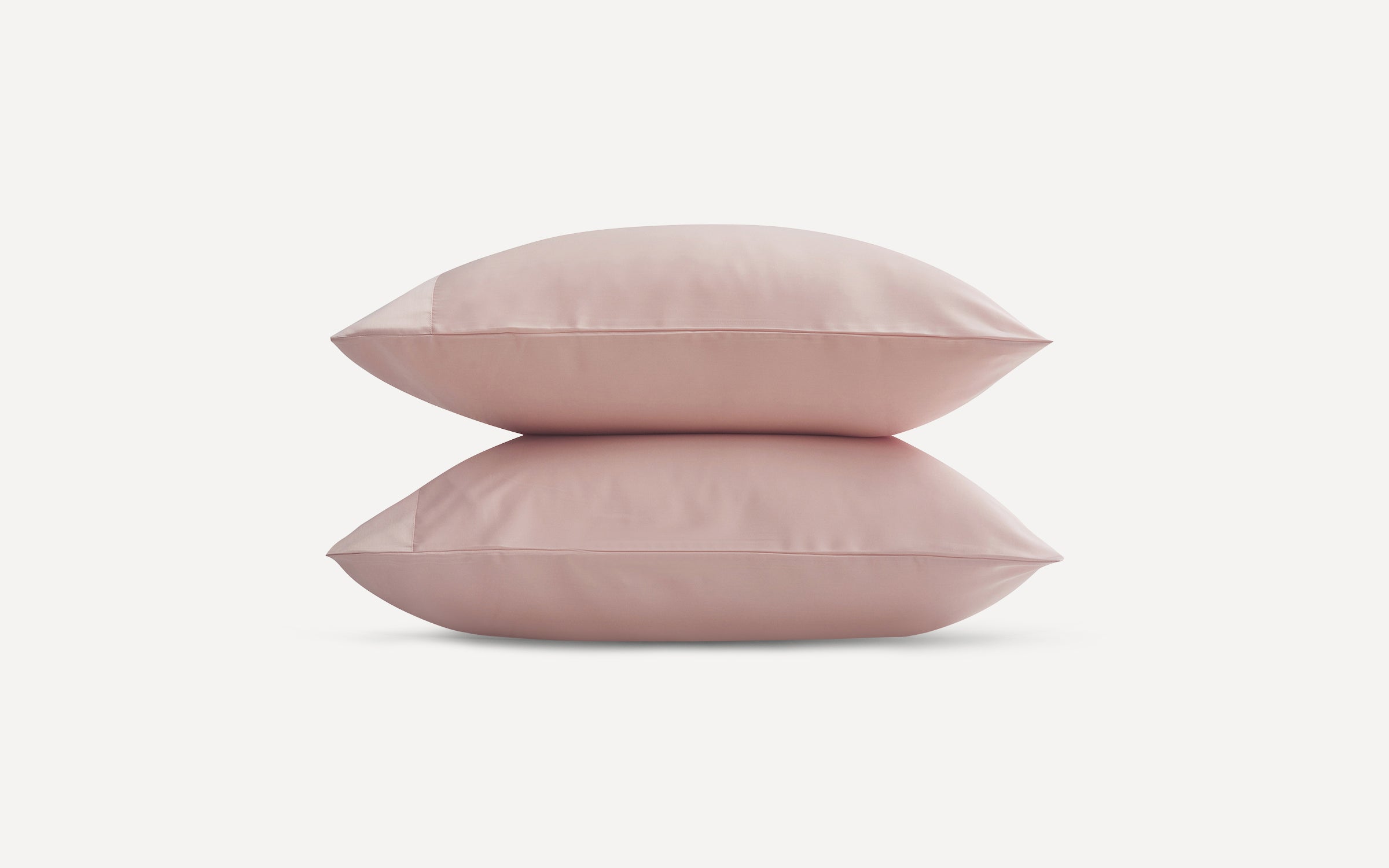 Two soft, light pink pillows stacked on a plain white background, showcasing smooth fabric texture.