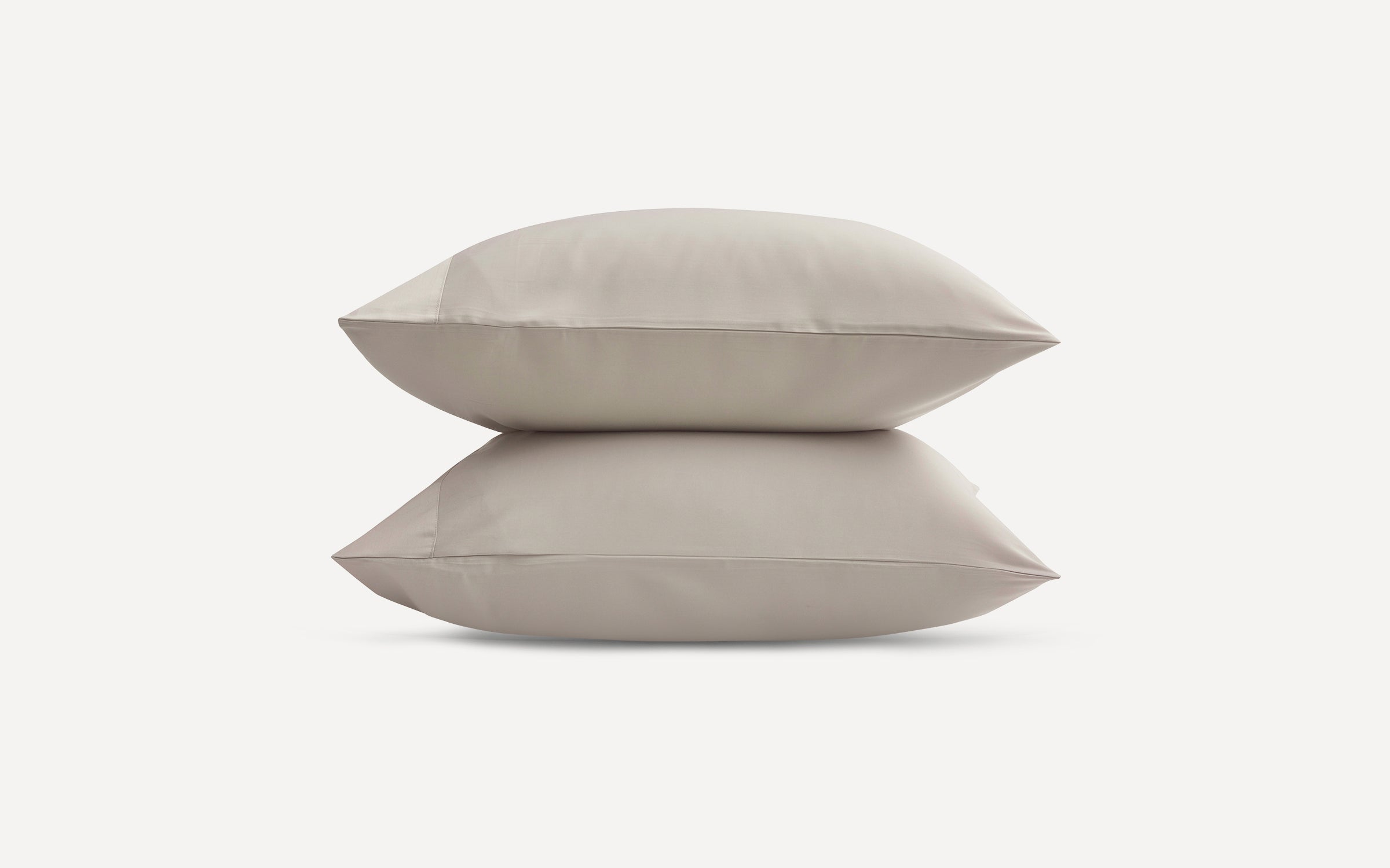 Two beige rectangular pillows stacked on a plain white background, showcasing smooth fabric and clean seams.