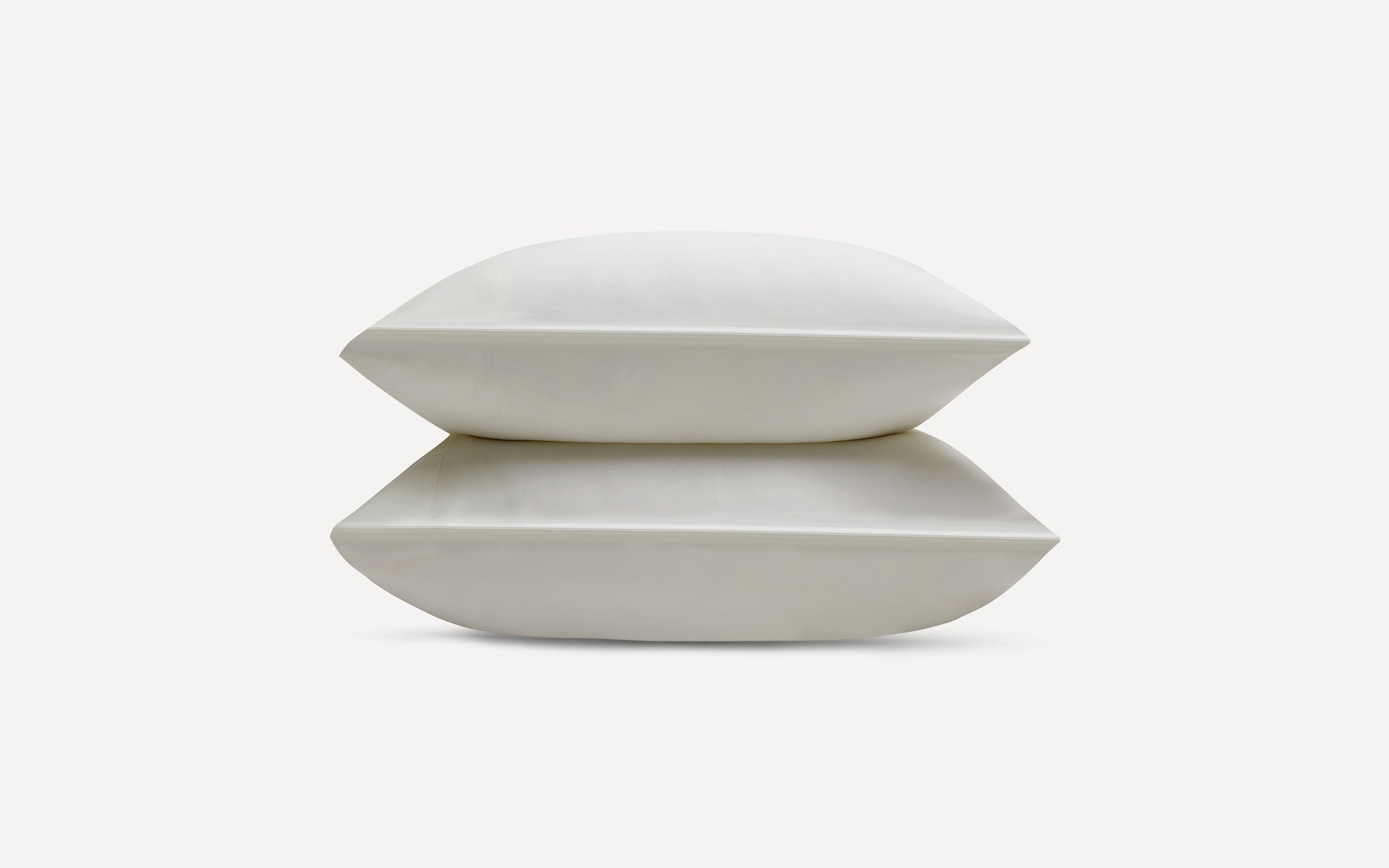Two stacked white rectangular pillows with smooth, clean fabric on a plain white background.