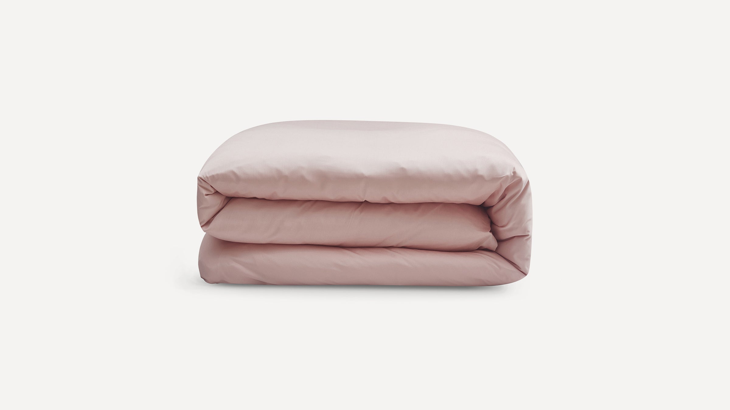 Light pink, neatly folded comforter or duvet on a plain white background, showcasing soft fabric texture.