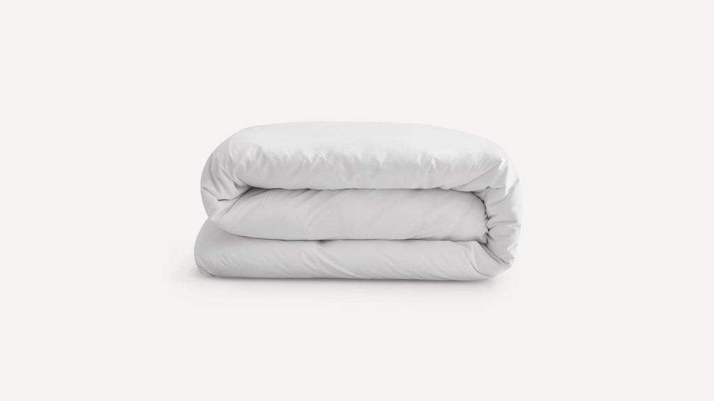 Neatly folded, plain white duvet or comforter on a white background, showcasing its soft and plush texture.