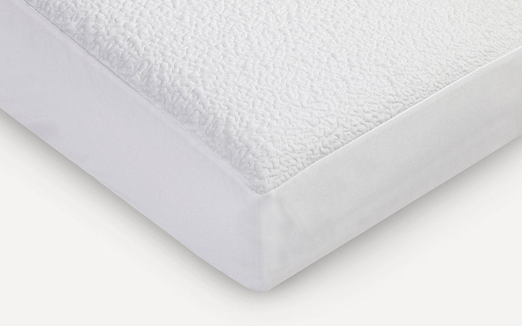 Close-up of a white mattress protector with a textured, quilted top layer and smooth fitted sides.