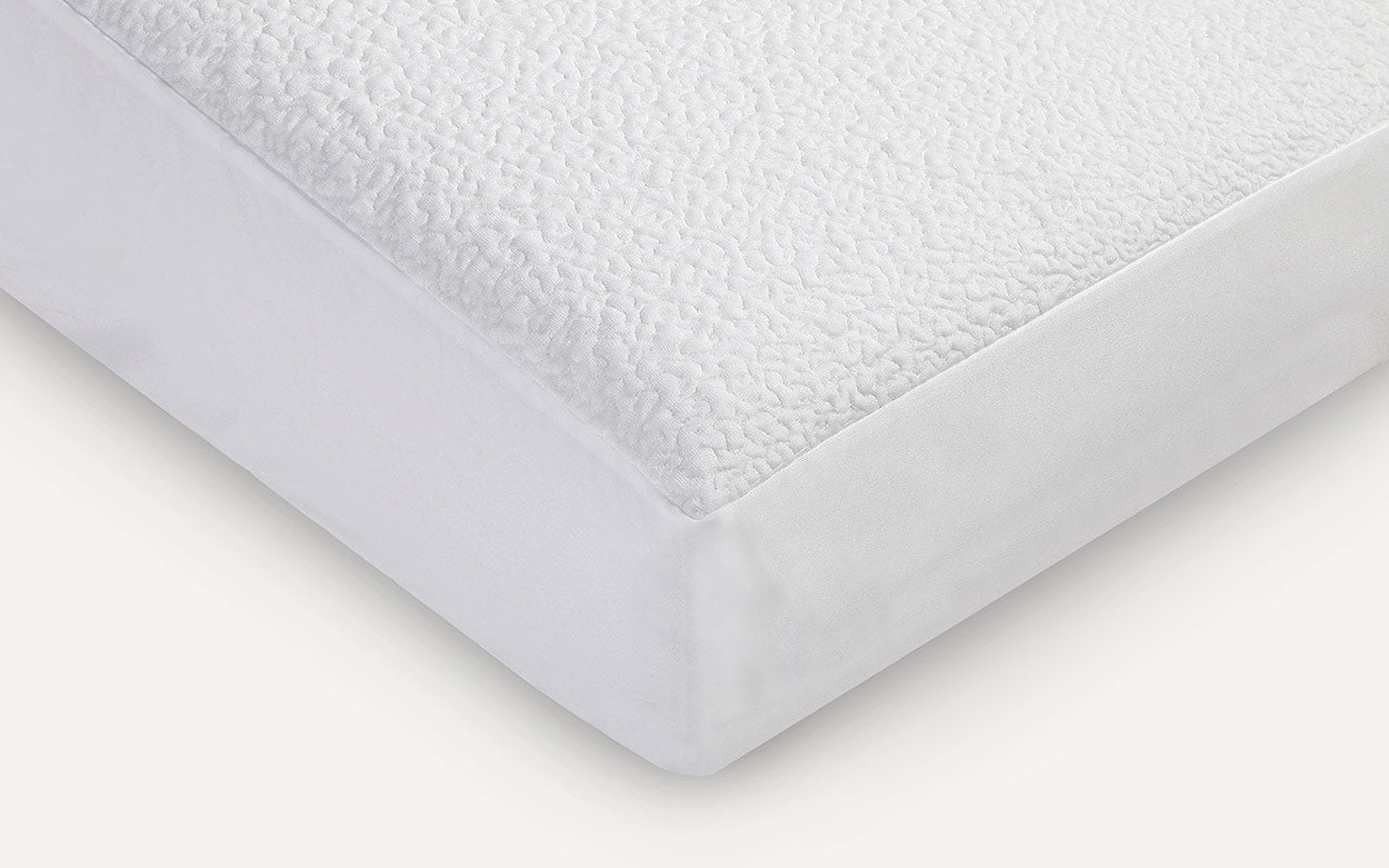 Close-up of a white mattress protector with a textured, quilted top layer and smooth fitted sides.