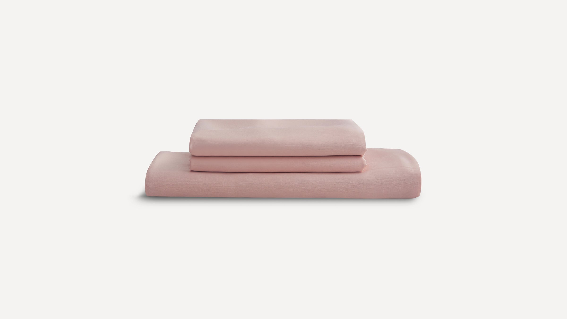 Stacked set of soft pink bed sheets and pillowcases folded neatly on a white background.