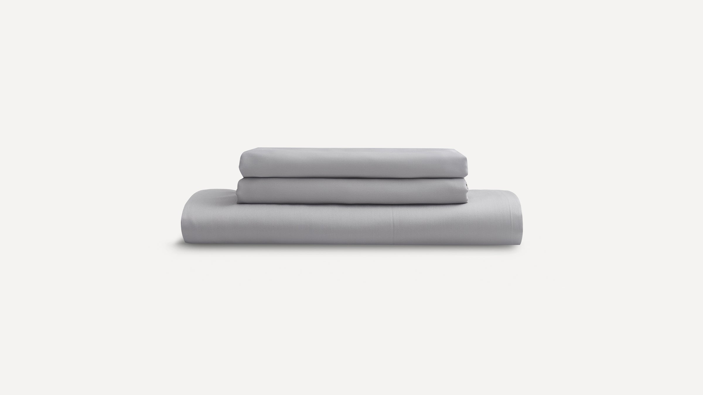 Stacked light gray bed sheets including a fitted sheet, flat sheet, and two pillowcases on a white background.