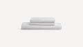 Stack of three neatly folded white bed sheets against a plain white background.