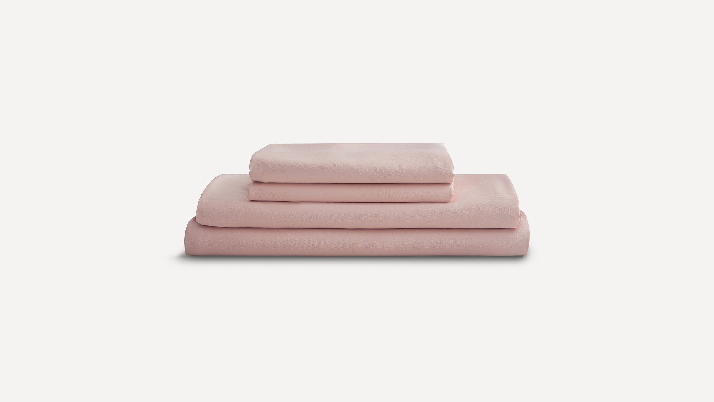 Folded set of blush pink bed sheets neatly stacked against a white background.