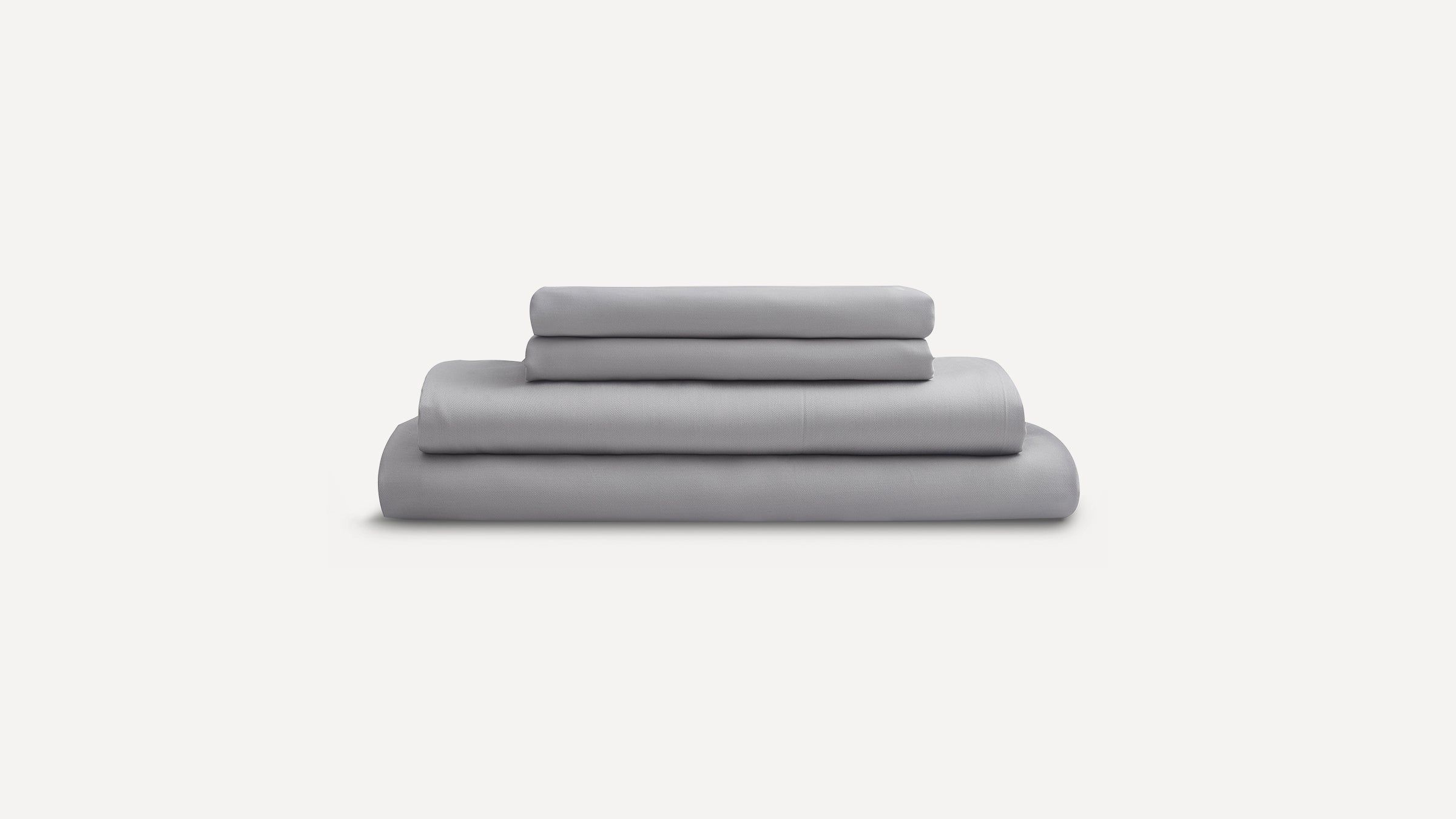 Stack of neatly folded light gray bed sheets and pillowcases on a plain white background.