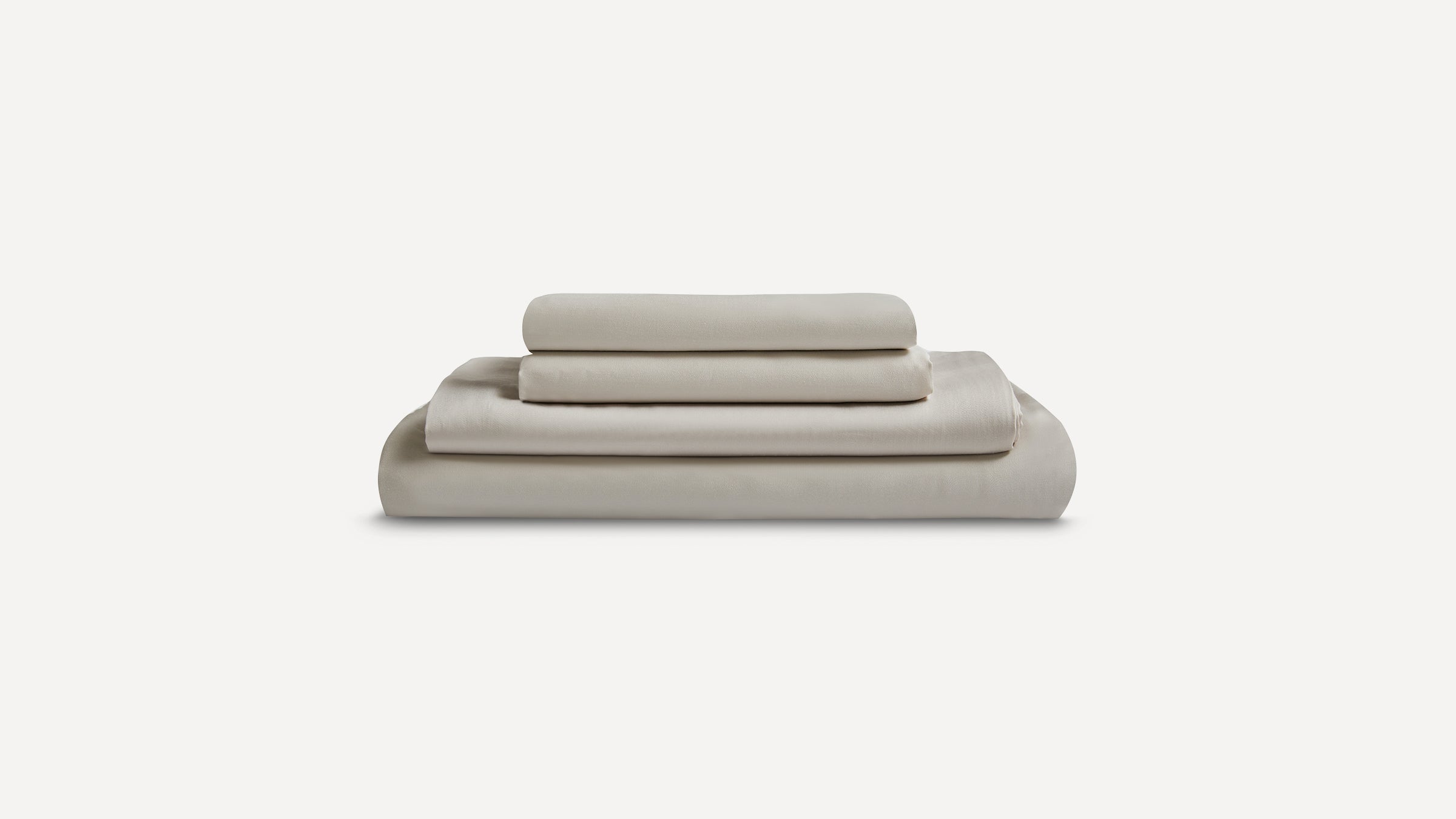 Set of four beige bed sheets and pillowcases neatly folded and stacked on a white background.