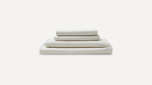 Stack of neatly folded white bed sheets and pillowcases on a plain light background.