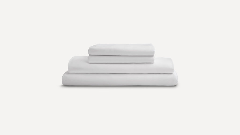 Stack of neatly folded white bed sheets and pillowcases on a plain light gray background.
