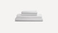 Stack of neatly folded white bed sheets and pillowcases on a plain light gray background.