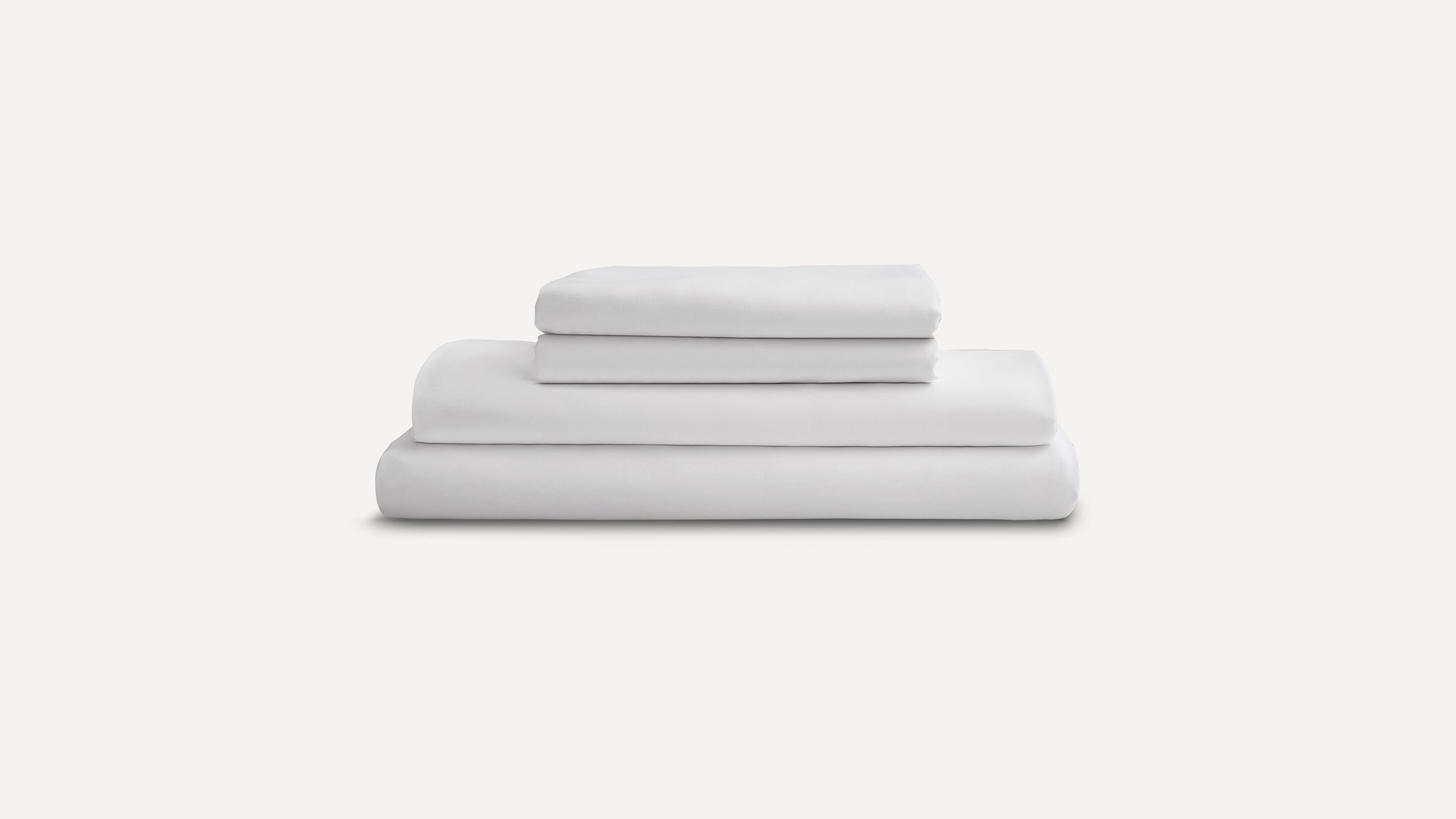 Stack of neatly folded white bed sheets and pillowcases on a plain light gray background.