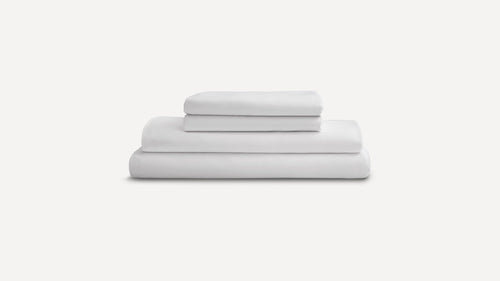 Stack of neatly folded white bed sheets and pillowcases on a plain light gray background.