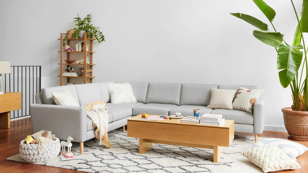modern living room with light gray sectional sofa, wooden coffee table, and white rug on the hardwood floor
