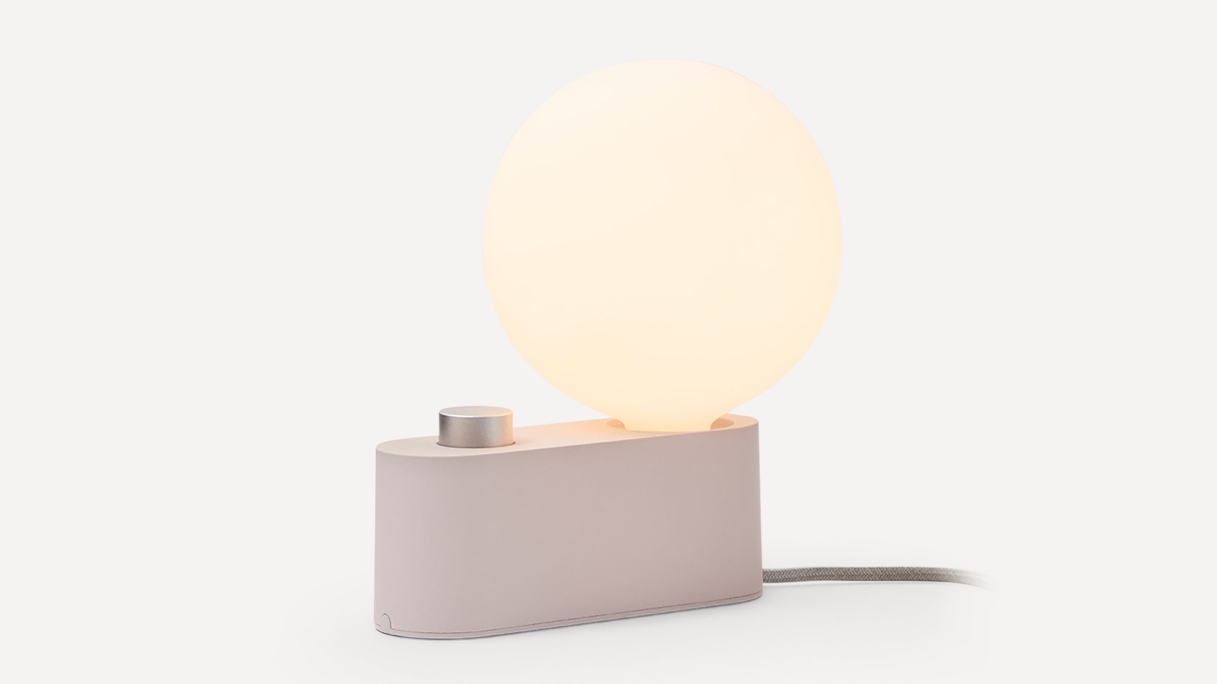 Modern table lamp with a glowing round white bulb, matte beige base, and a silver knob, on a white background.