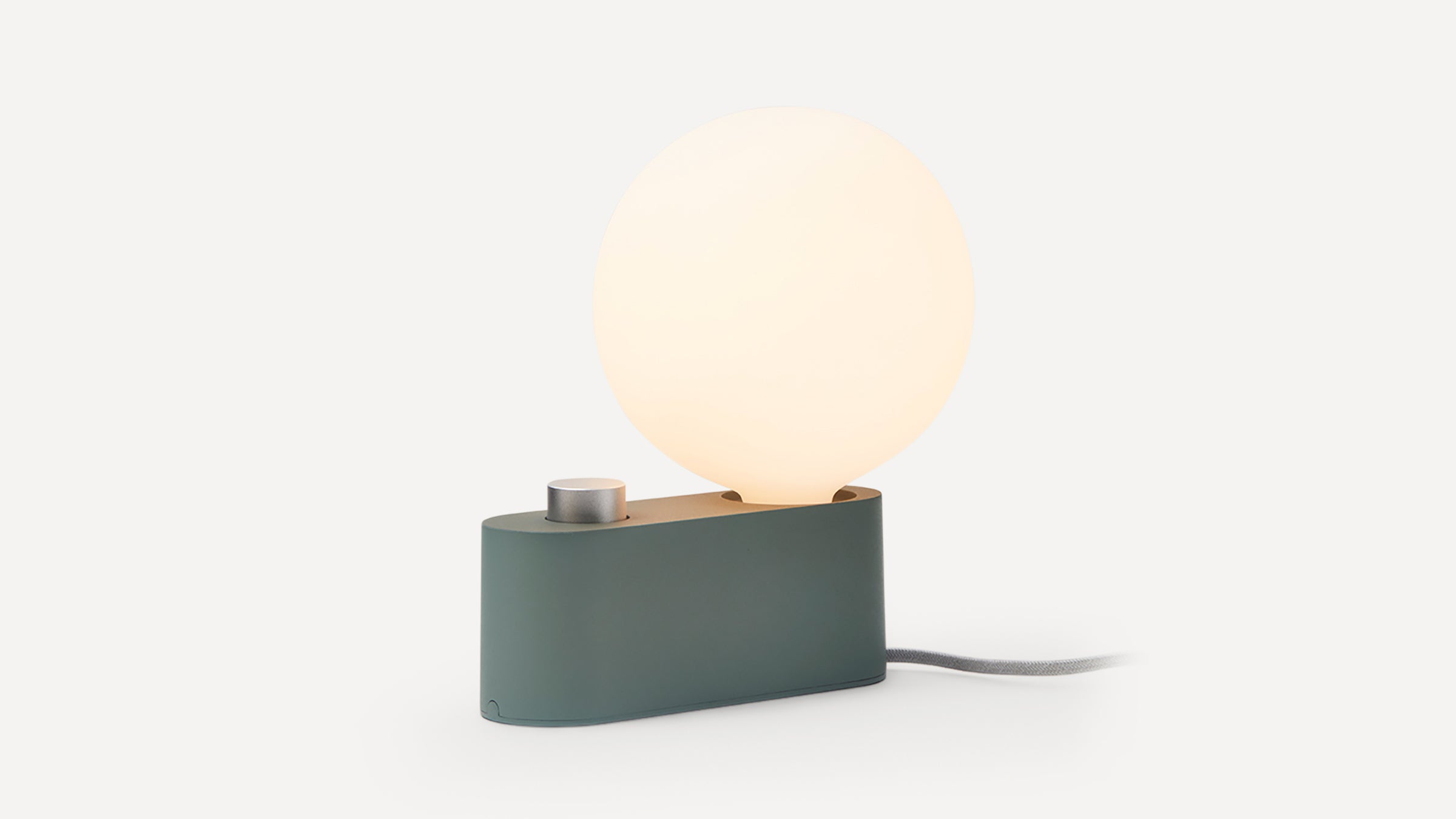 Modern desk lamp with matte green base, large glowing round bulb, and metallic control knob, set against white background.